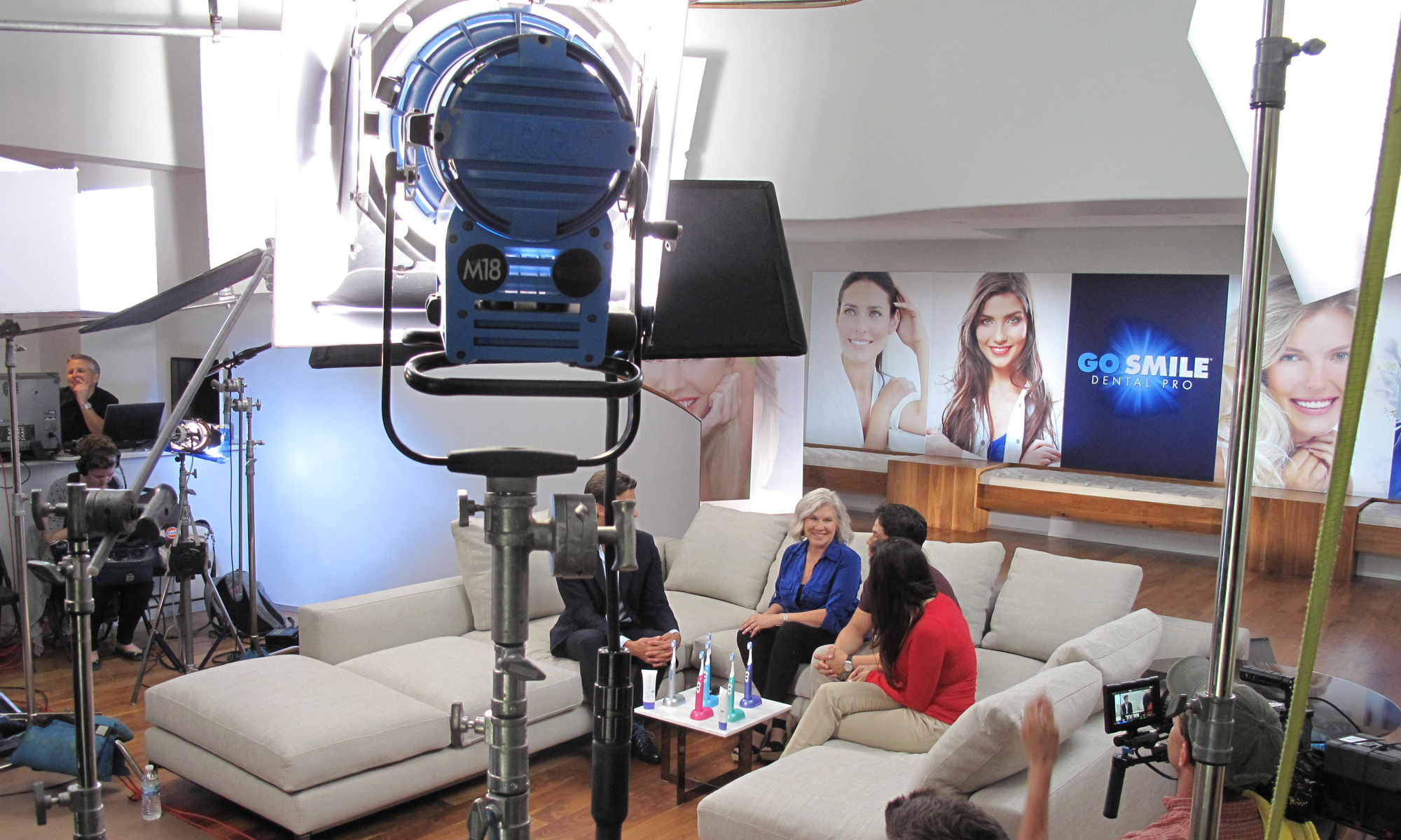 Location shot of in-house studio setting. Several people sitting in living room setting discussing Dental Pro products. M18 Light sit in foreground while other stands, flags and boxes are being used. Gaffer Lighting Truck Dallas